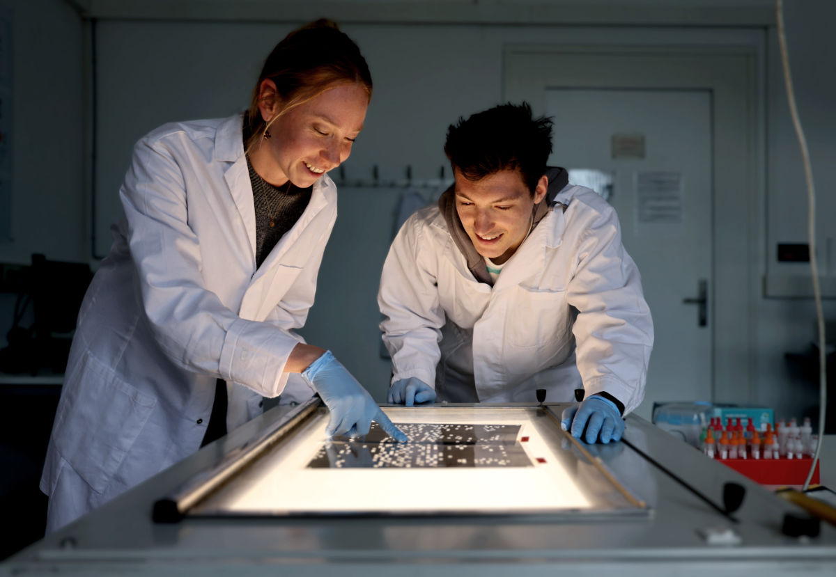 Zwei Studierende in einem abgedunkelten Raum, die etwas an einer Lichtquelle untersuchen